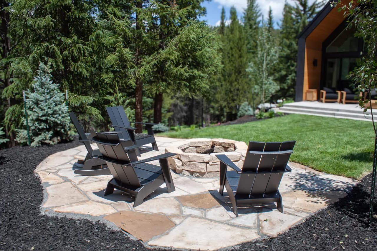 Flagstone patio with a stone fire pit and black Adirondack chairs beside a cabin
