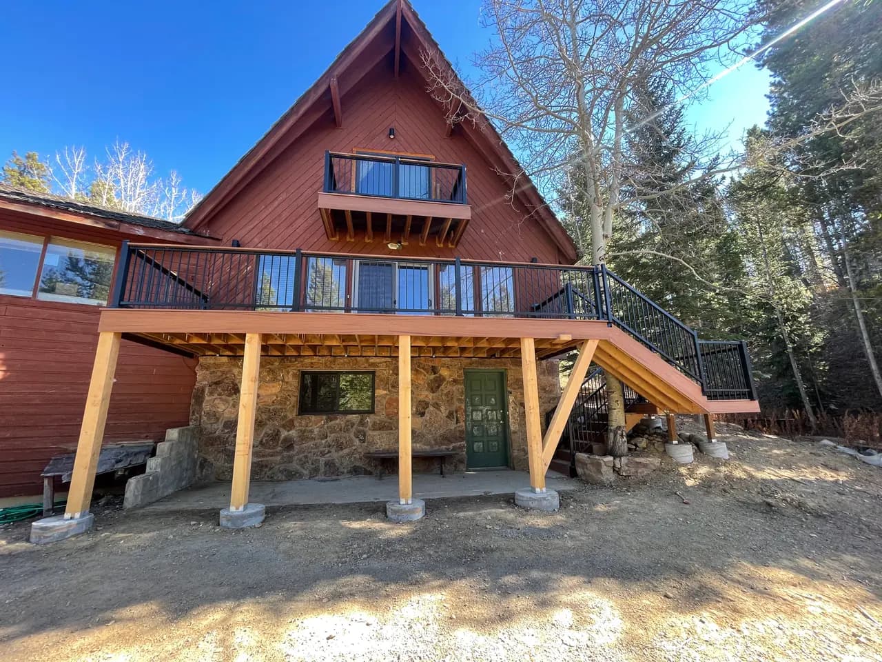 A-frame cabin with a new wraparound deck on timber posts above a stone patio