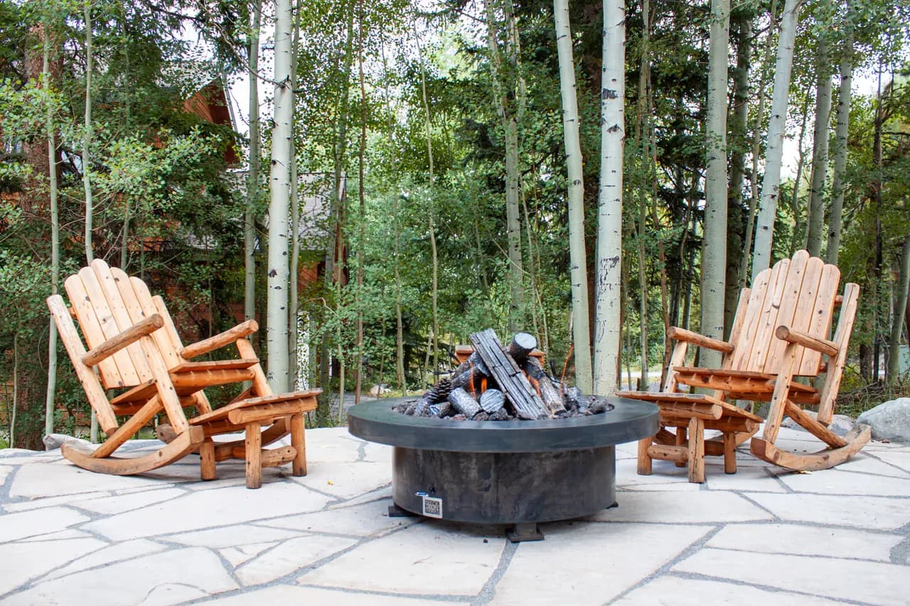 Flagstone patio with a round fire pit and log rocking chairs in an aspen grove