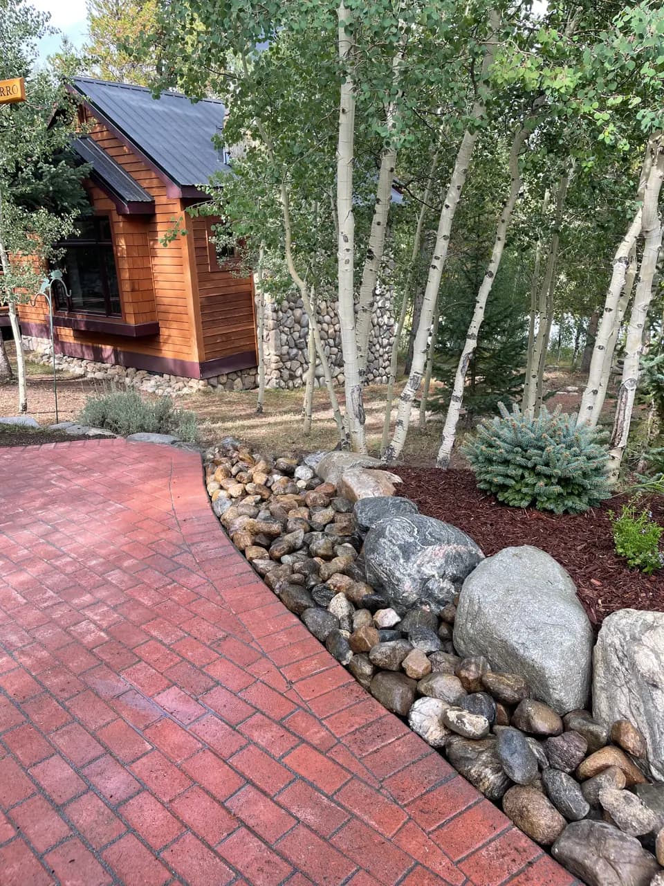 Curved brick paver walkway edged with river rock and boulders in front of a cabin